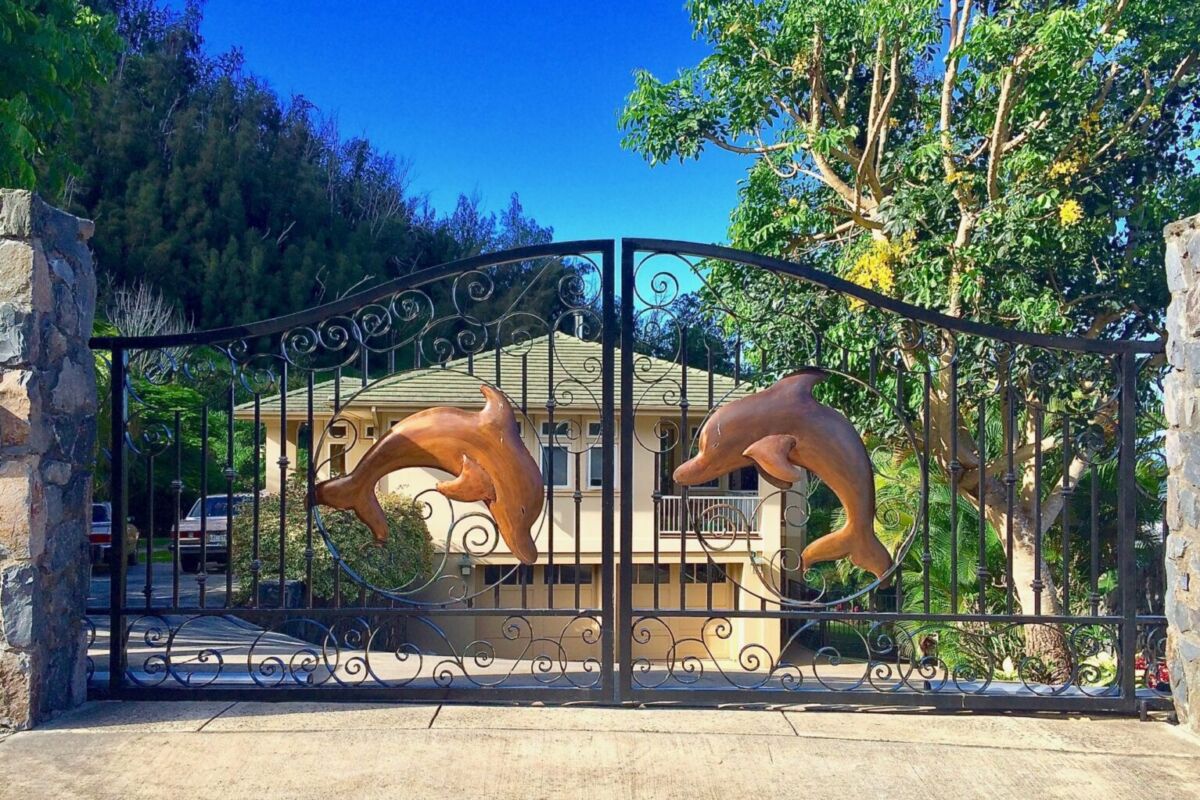 Decorative dolphins mounted on a black metal gate in a sunny outdoor setting.
