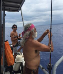 Two men fishing on a boat under a cloudy sky.