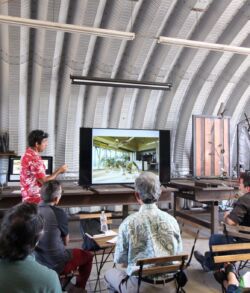 People attending a presentation in a rustic indoor setting with a projector screen.