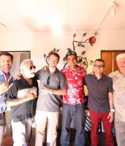 A group of six men posing together in a warmly lit room.