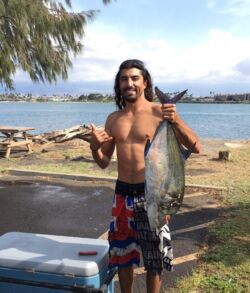 Man proudly holding a large fish near the beach.