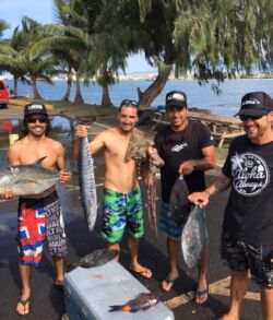 Four men proudly holding large fish on a sunny day near the ocean.