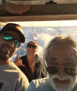 Three people smiling on a boat with water in the background.