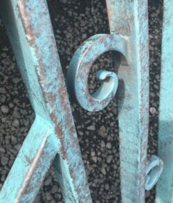 Close-up of a weathered turquoise wrought iron fence with decorative scrollwork.