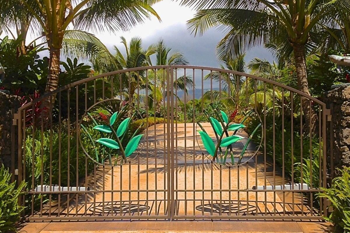A gated entrance with lush tropical plants and a distant view of the ocean.