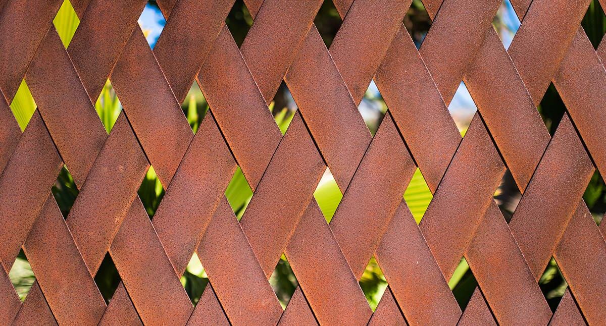 Close-up of a brown wooden lattice fence with small gaps revealing greenery.