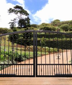 A black iron gate in front of a landscaped garden and pathway.