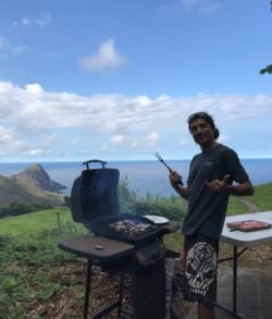 Man grilling food outdoors with a scenic ocean view in the background.