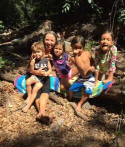 Four children sitting on a log in a forest, smiling and enjoying nature.