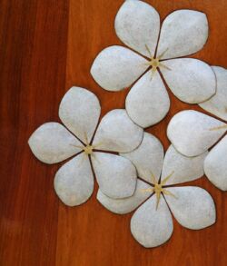 Copper and brass Plumeria inlay White flower-shaped coasters on a wooden surface.