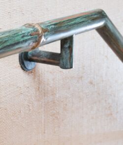 Custom green patina finish with brass bamboo highlights Rusty metal handrail mounted on a wall with a beige background.