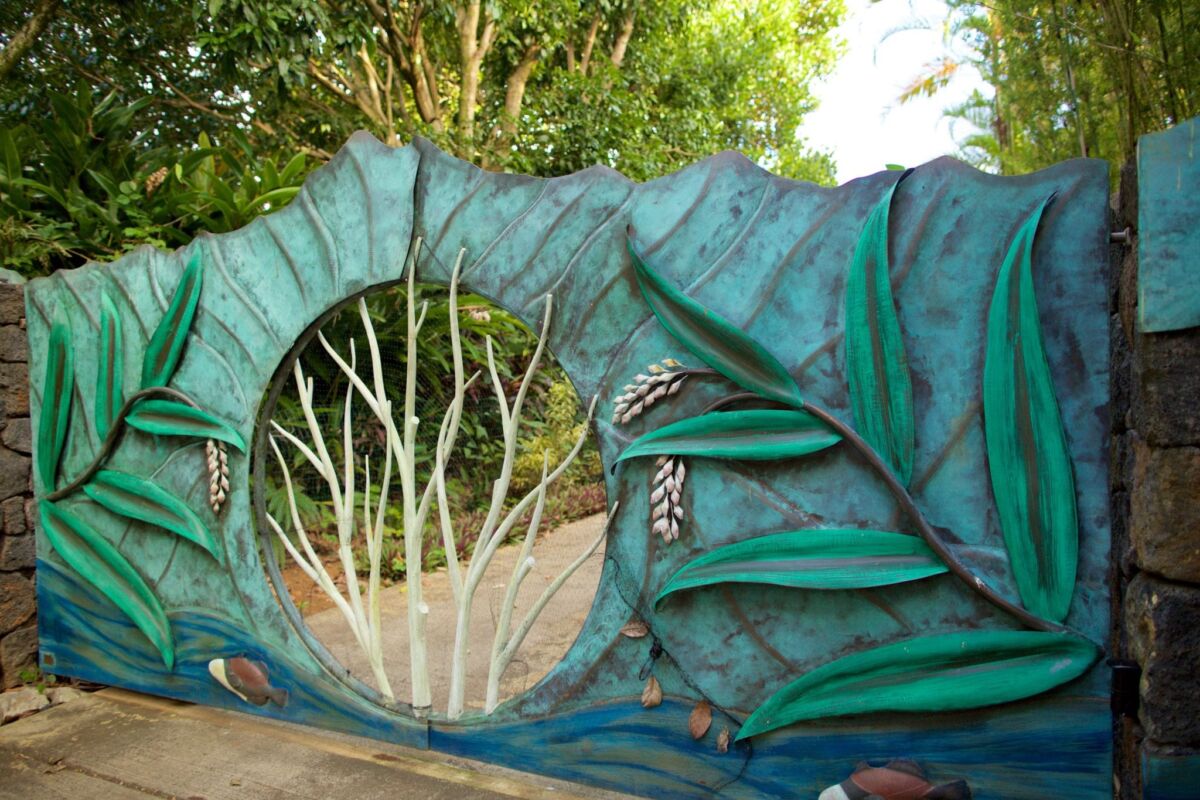 A green dragon sculpture with an open mouth and visible teeth in a garden.