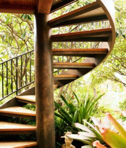 A wooden spiral staircase surrounded by greenery and flowers.
