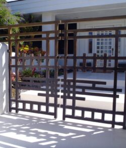 Decorative metal gate with geometric patterns in a sunny courtyard.