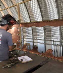 A person welding metal inside a curved metal structure.