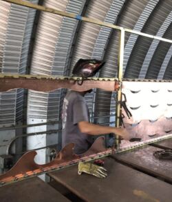 A worker welding metal bars inside a metal shed.
