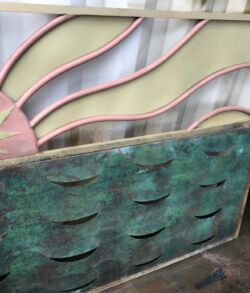 Artistic panels with sun motif and textured green design leaning against a wall.