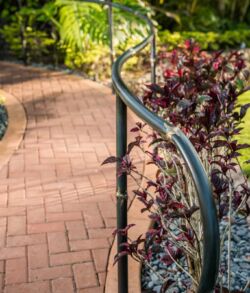 Curved metal railing alongside a brick pathway with purple plants.