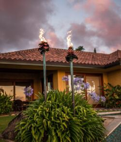 Two flaming tiki torches light up a tropical garden at sunset.