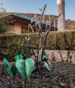 Metal sculpture of a tree with green leaf-shaped accents in a garden.
