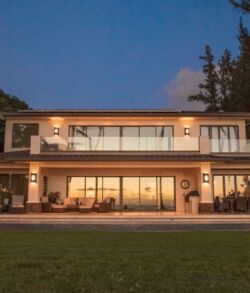 Modern two-story house illuminated at dusk with large windows.