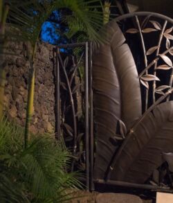 Artistic metal gate with leaf and bamboo designs at night.