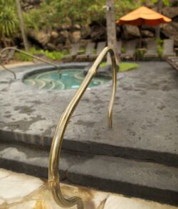 Rusty metal handrail by a small outdoor pool or hot tub.