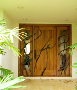 Wooden entrance door with artistic metalwork of two figures and a trident.