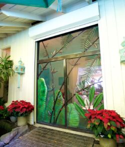 Floral bamboo entry door Decorative stained glass door framed by plants and red flowers.