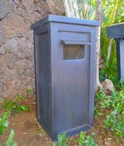 A rustic black mailbox with a mail slot on a stone background.