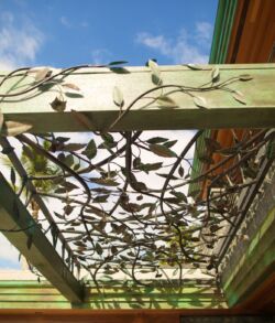 Floral patio shade trellis Decorative metal panel with leaf motifs under a wooden pergola.