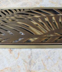 Decorative metal grate with a leaf pattern on a stone surface.