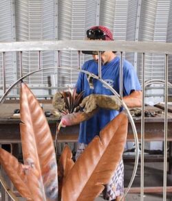 A person working with tools inside a workshop behind a decorative metal fence.
