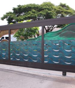 Modern metal gate with geometric cutouts and a green mesh behind it.