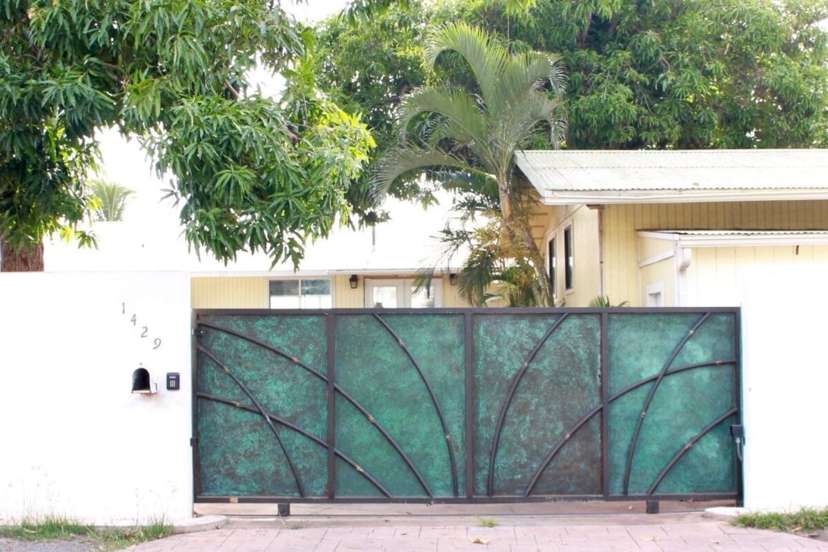 Green metal gate with geometric design in front of a house.