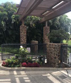 Stone pillars supporting a pergola over a garden entrance with lush greenery.