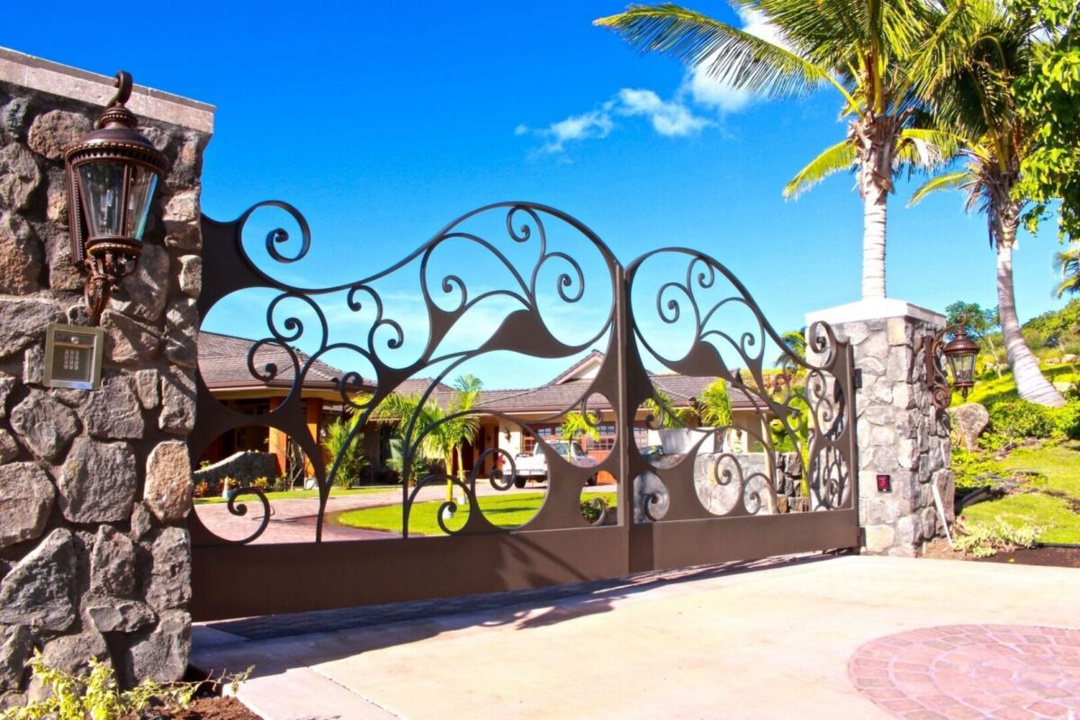 Elegant wrought iron gate with palm trees under a clear blue sky.