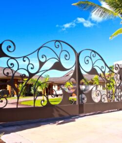 Elegant wrought iron gate with palm trees under a clear blue sky.