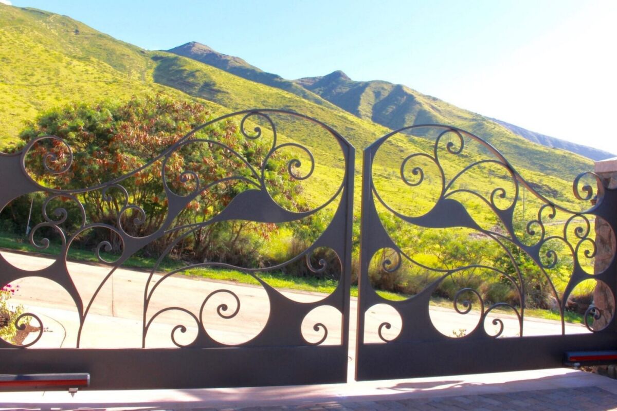 Ornate iron gate overlooking sunlit mountains and greenery.