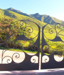 Ornate iron gate overlooking sunlit mountains and greenery.