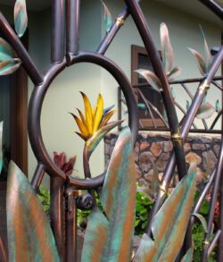 Detailed close up shot. Metal fence with leaf designs and a bird-of-paradise flower behind it.