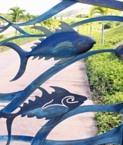 Metal fish sculptures on a blue fence with greenery in the background.