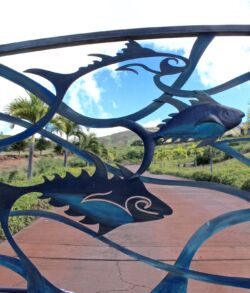 Decorative metal shark sculptures on a garden fence with a scenic background.