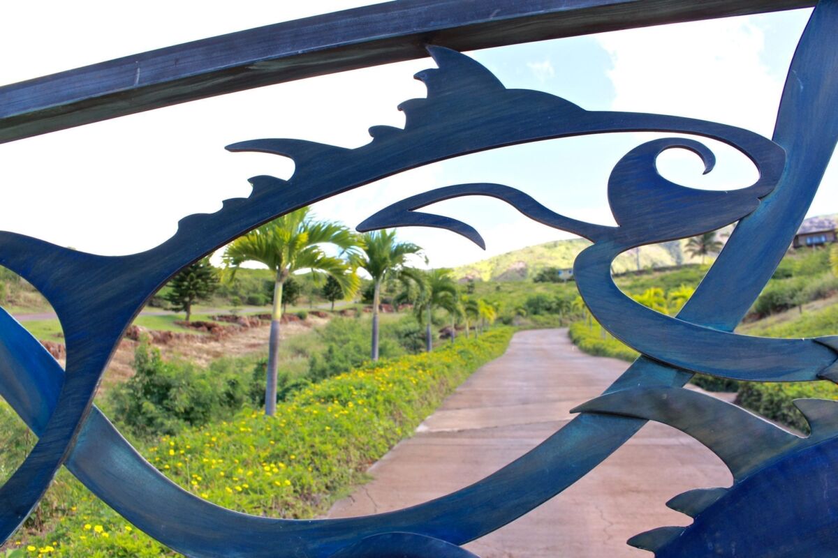 Decorative metal fish sculpture overlooking a scenic rural path with palm trees.