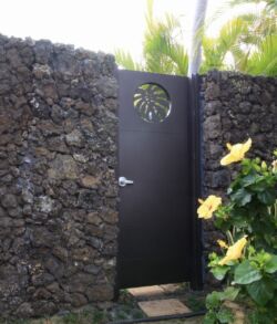 Black metal gate with a star cutout in a stone wall surrounded by greenery.