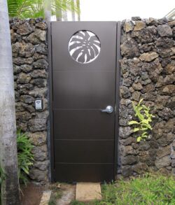 Modern metal door set in a rustic stone wall with greenery.