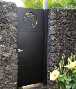 Black metal gate with a circular design, set between stone walls and surrounded by greenery.