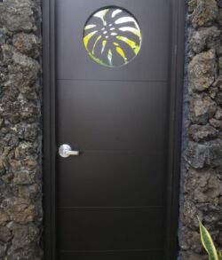 Dark wooden door with a round window featuring a leaf design, set in a stone wall.