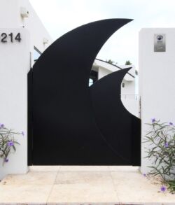 Modern black crescent-shaped gate on a white wall with plants.