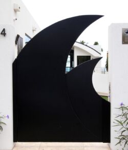 Modern black gate with crescent moon design in white wall.